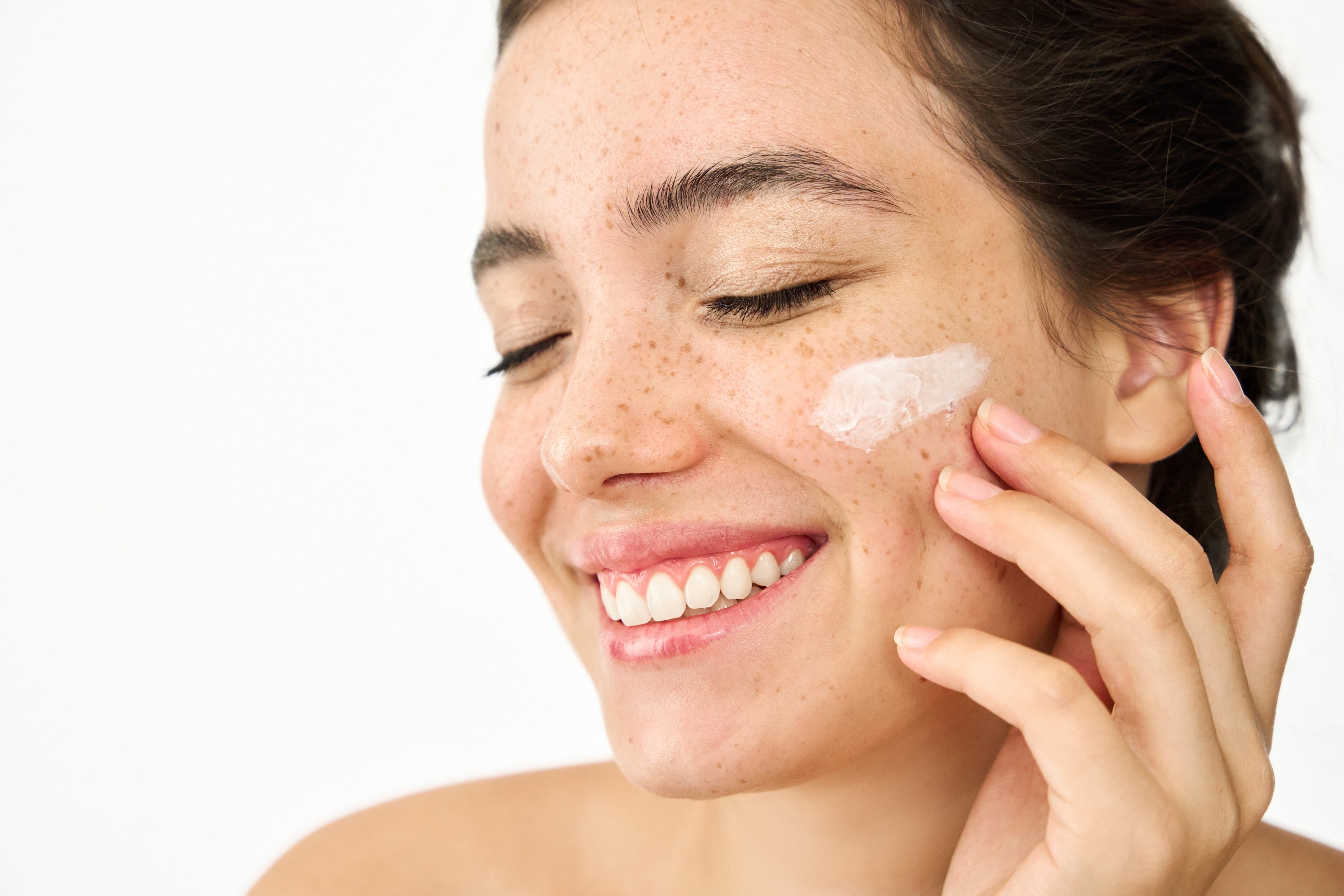 Woman smiling while applying moisturiser to freckled skin, part of the Clear Skin Membership at McQuarrie Skin & Beauty in Havelock North, Hawke's Bay
