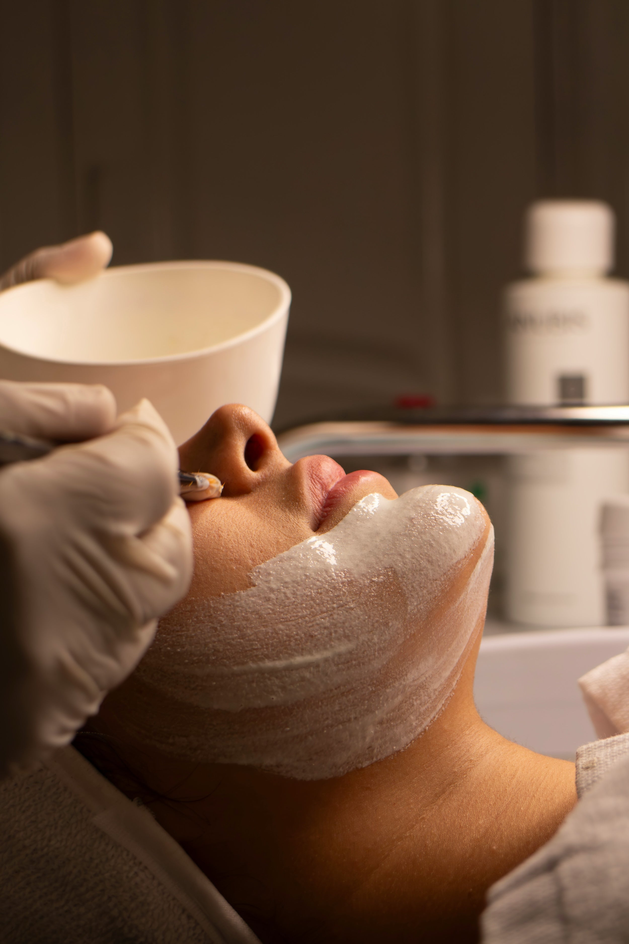 Person receiving a facial treatment for the Depigmentation Package at McQuarrie Skin & Beauty, shown with white treatment on their face and the therapist is wearing gloves.